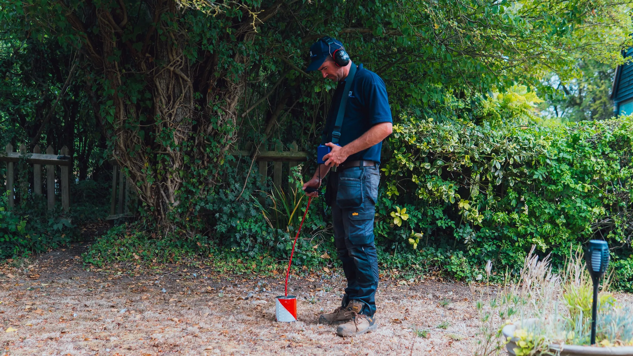 ADI engineer in a garden holding a tracer gas detector wand over a small marker on bare ground