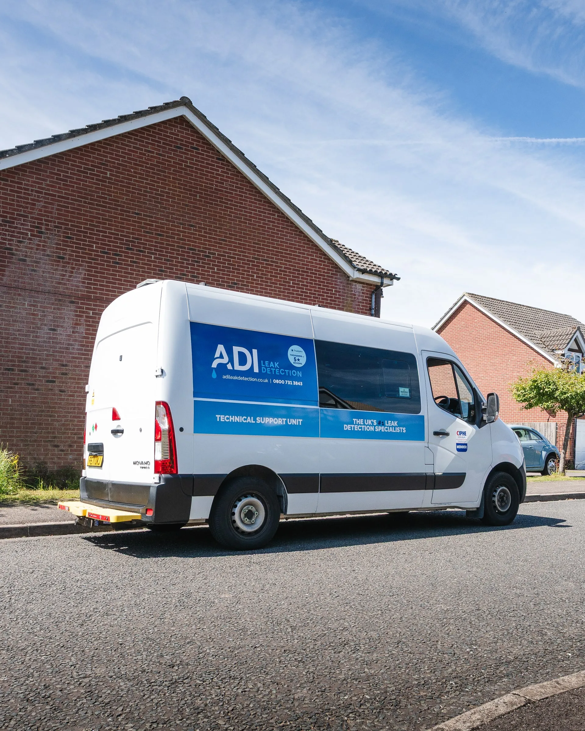 ADI Leak Detection van parked on a street beside modern brick houses under a blue sky